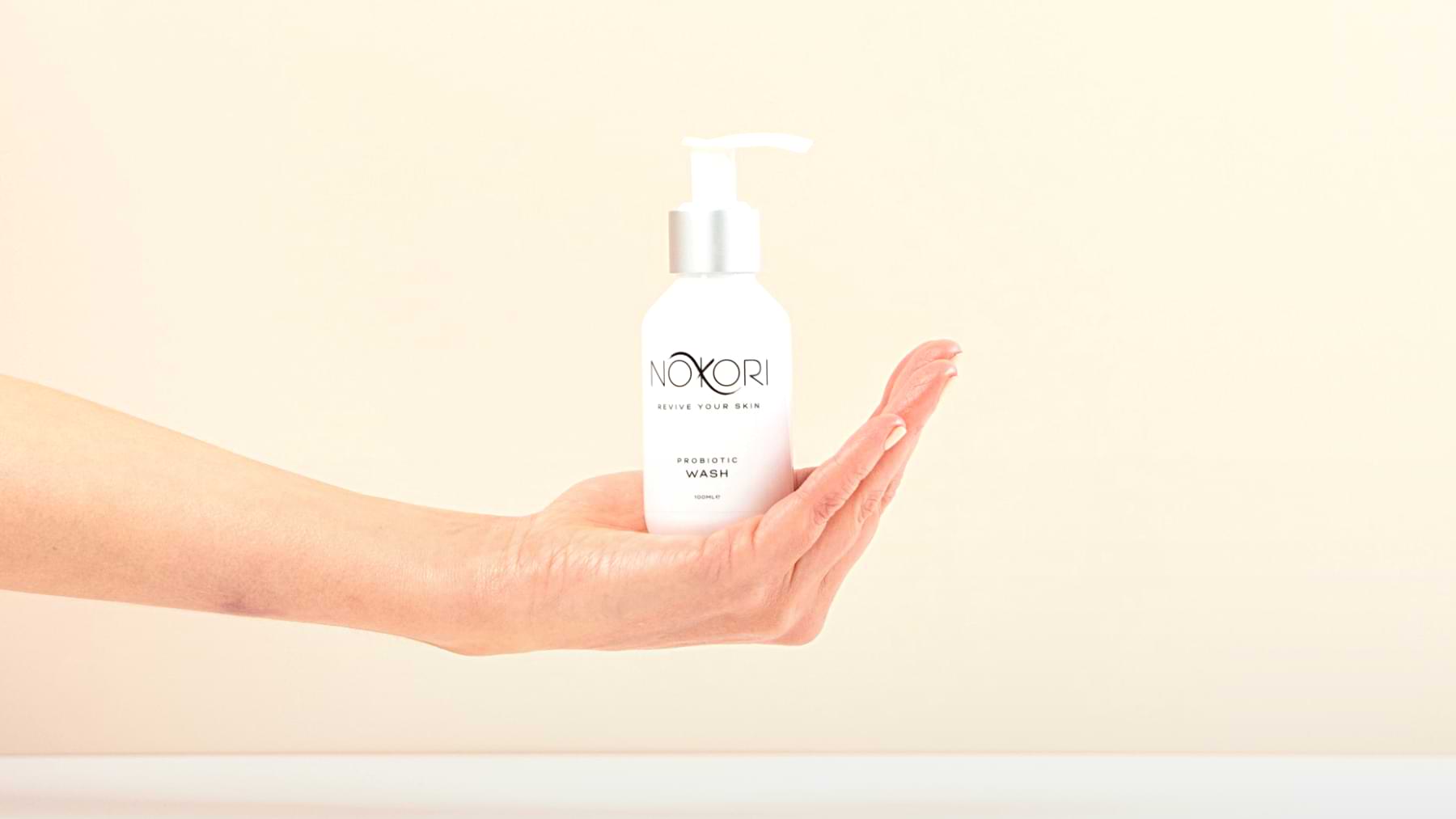 A bottle of Nokori Probiotic Wash balanced upright on an open palm, set against a soft beige background.