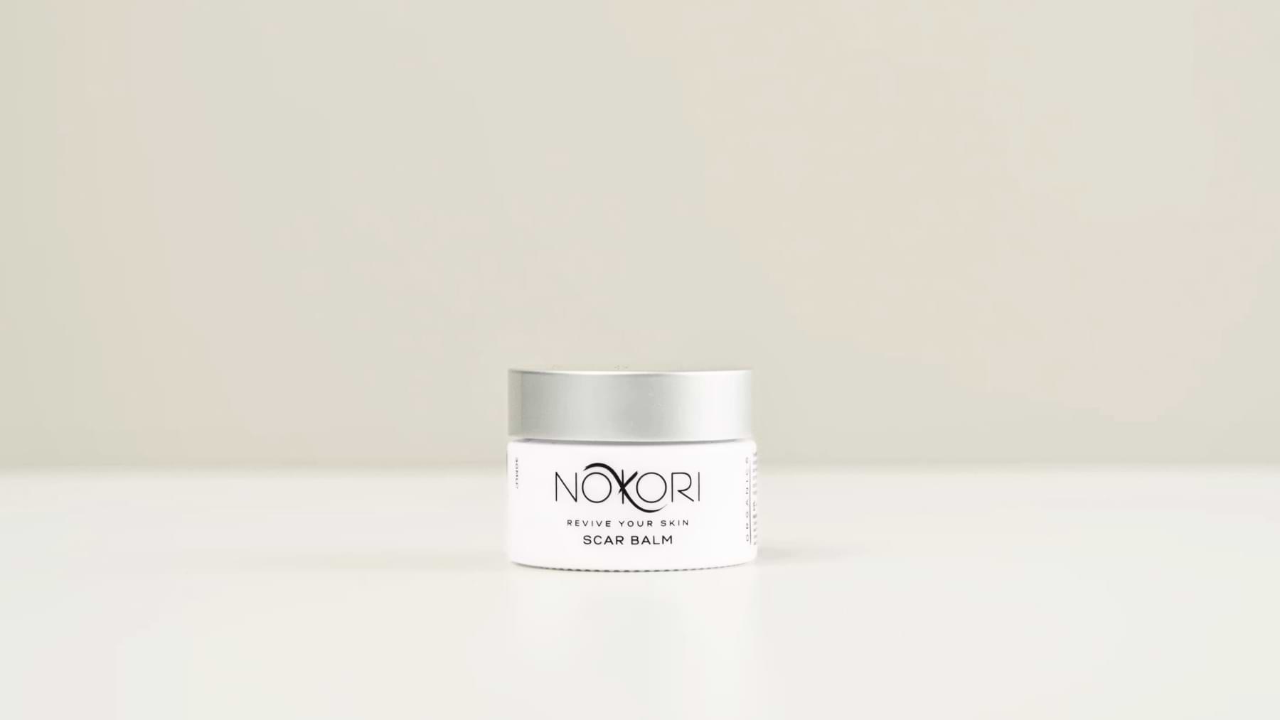 A standalone jar of Nokori Scar Balm displayed against a pale, minimal backdrop.