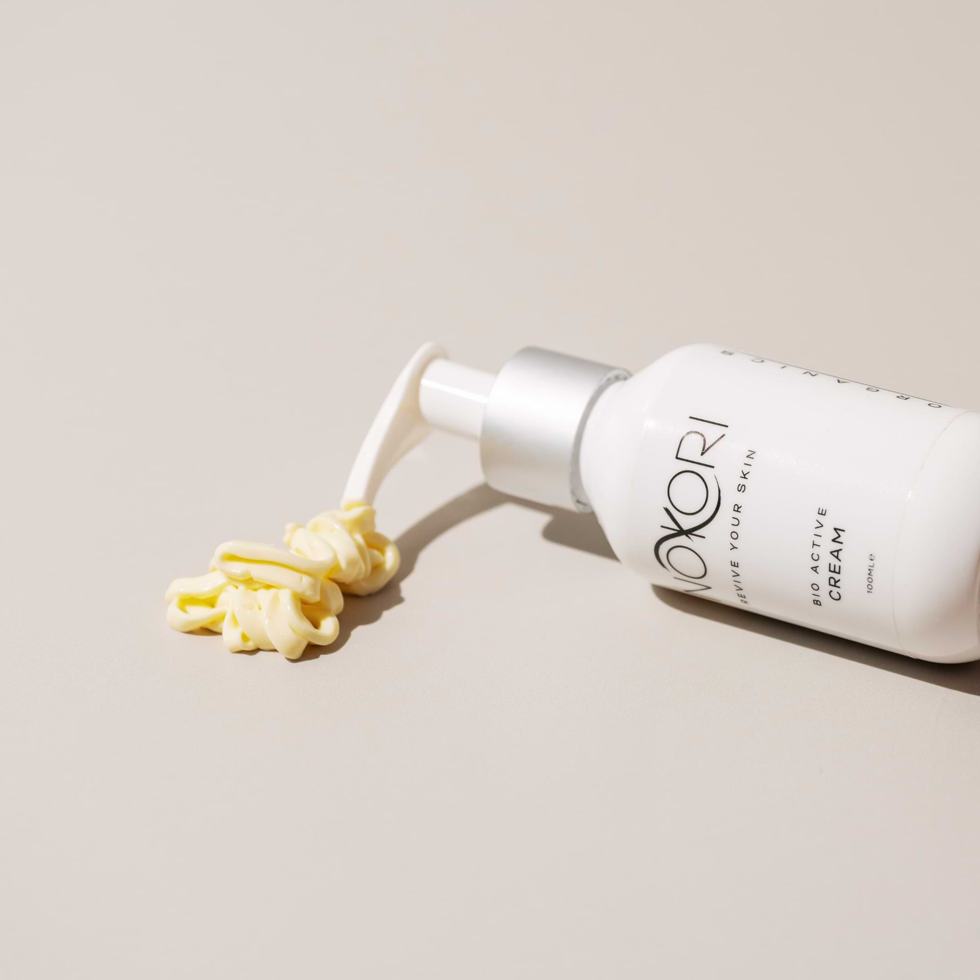 Nokori Bio Active Cream lying on its side with cream dispensed in a neat swirl on a beige surface