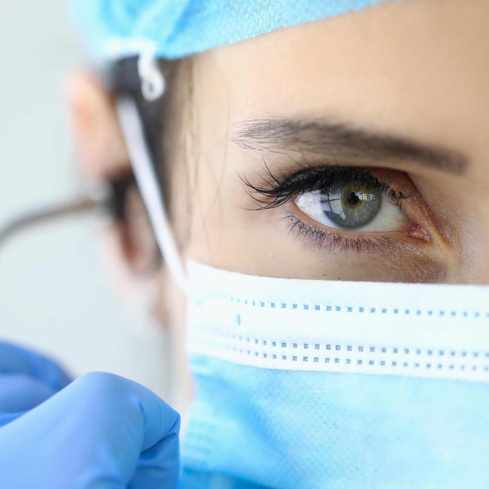 Close-up of a healthcare professional’s eye, wearing a surgical mask and cap—focused and attentive during patient care.