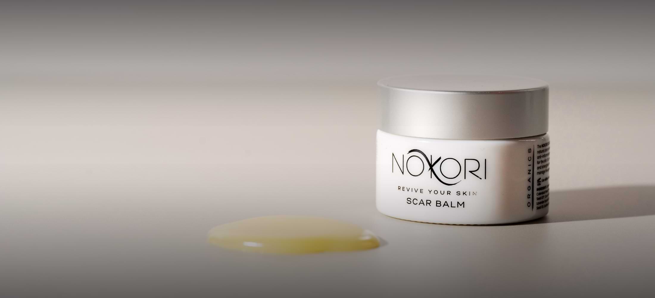 Nokori Scar Balm jar with balm gently spread beside it — showcasing product texture in soft, natural lighting.