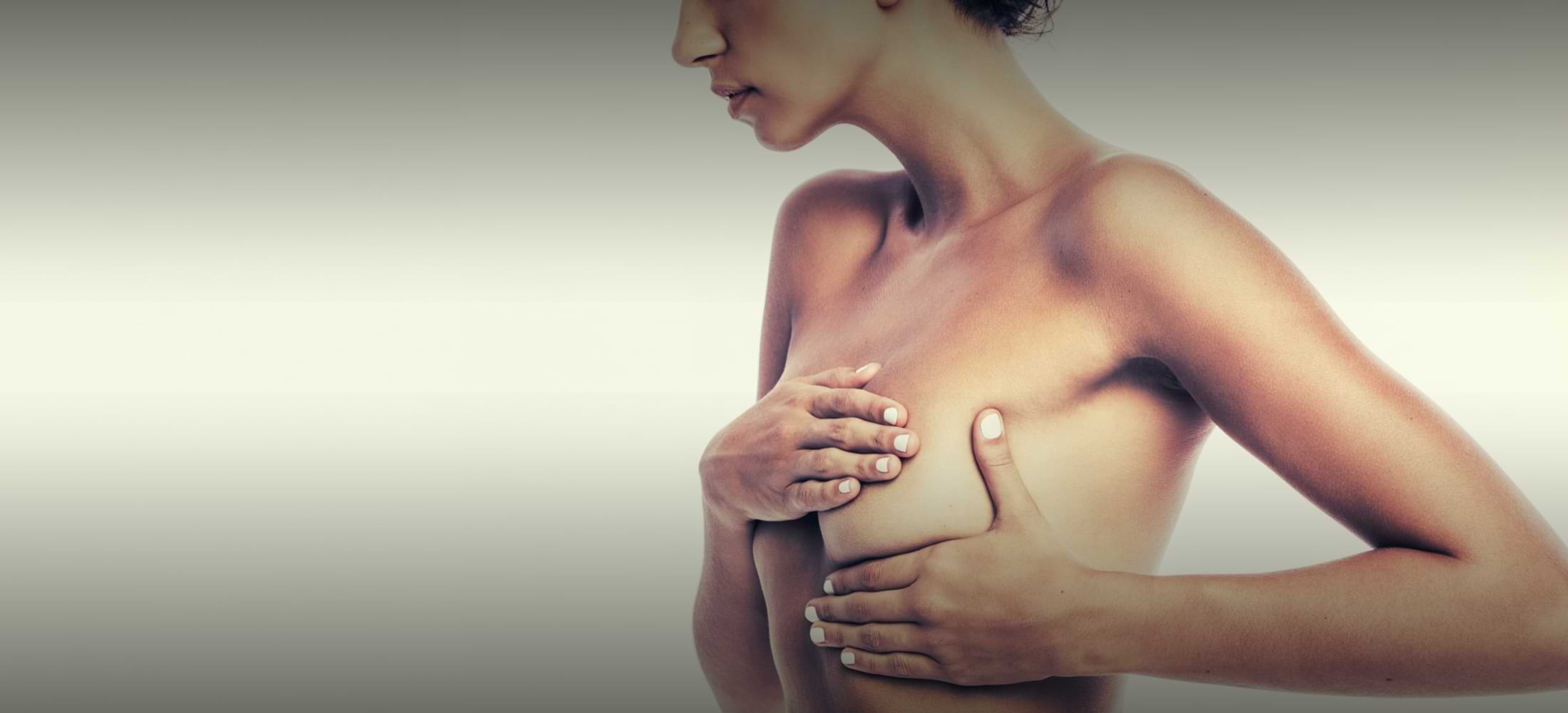 Side view of a topless woman gently cupping her breasts — a quiet, empowered moment of post-surgical self-care.