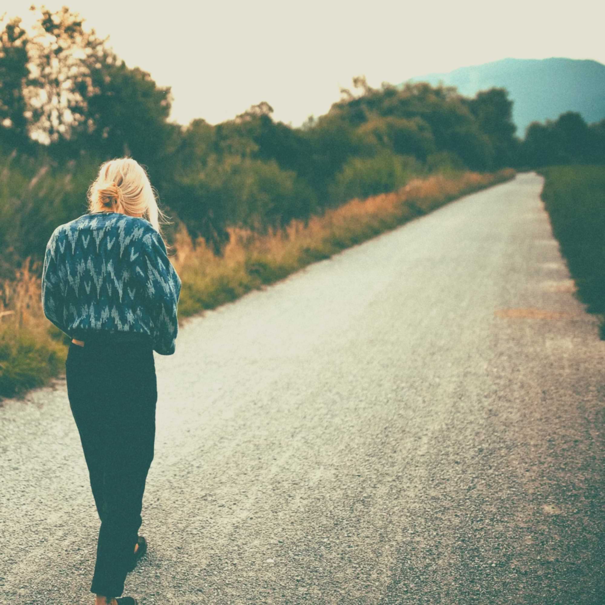 Woman walking alone on a country road, surrounded by nature—reflective and calm.