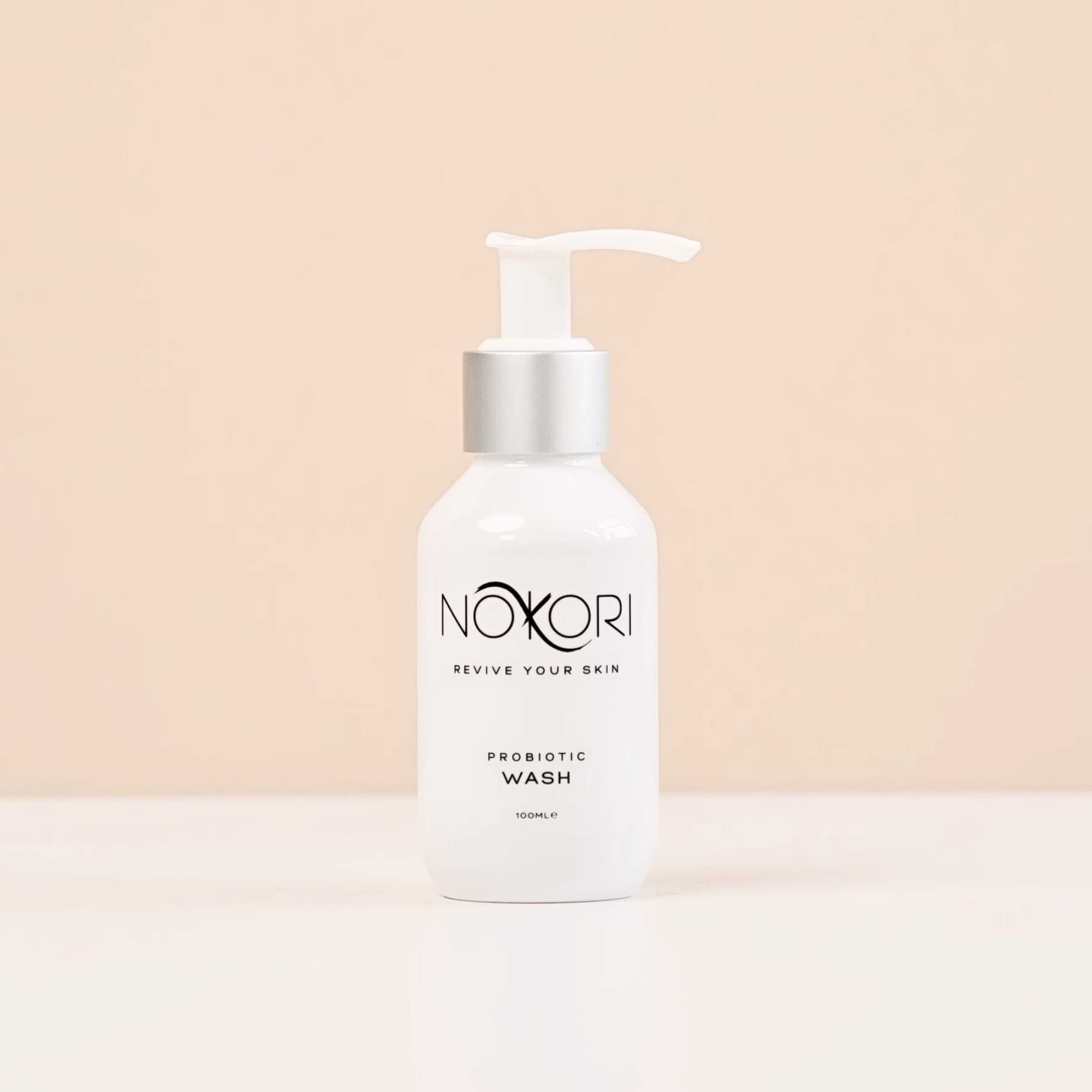 A white bottle of Nokori Probiotic Wash with a silver pump top, standing against a soft peach background.