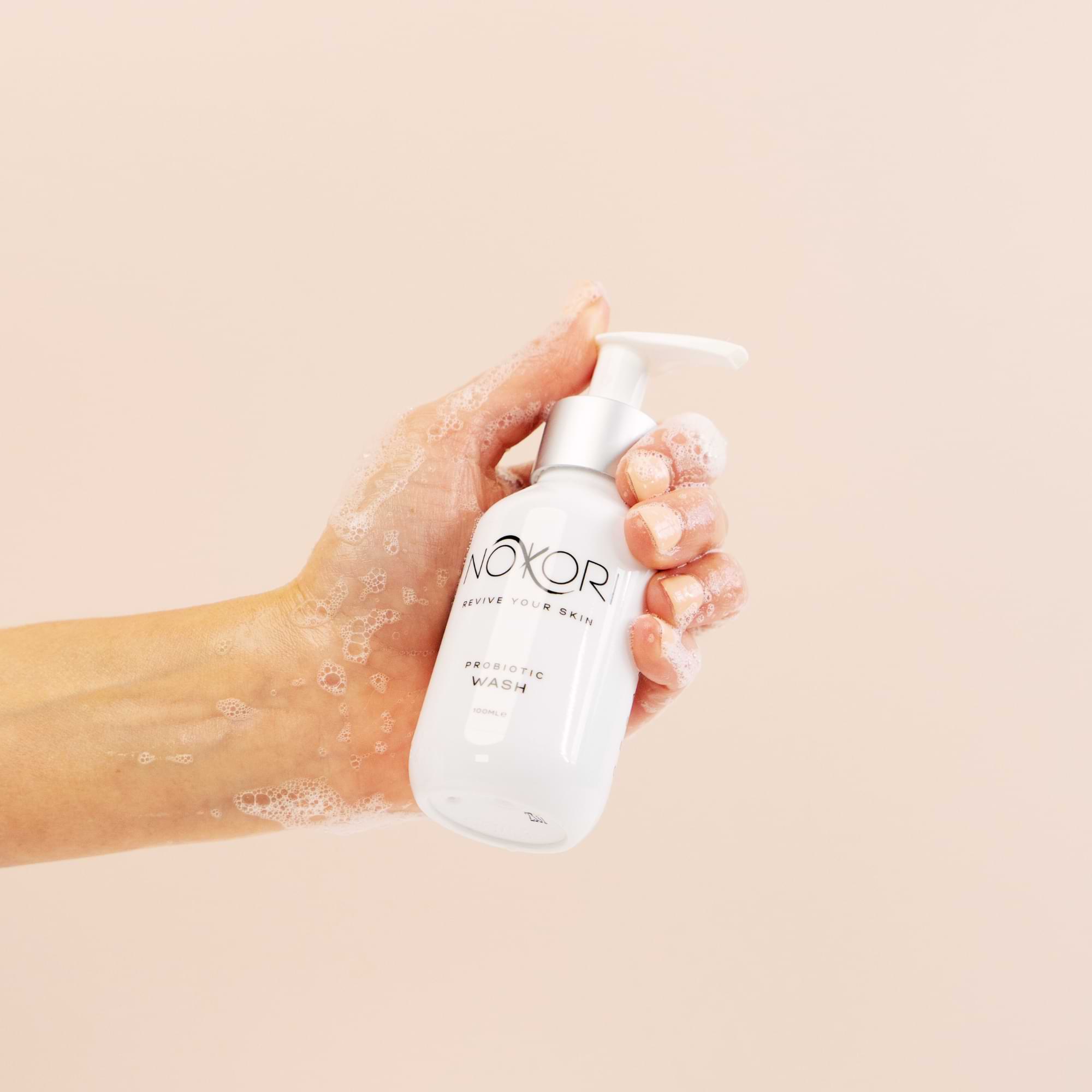 Hand holding a foamy Nokori Probiotic Wash bottle, suggesting lather and cleansing use.