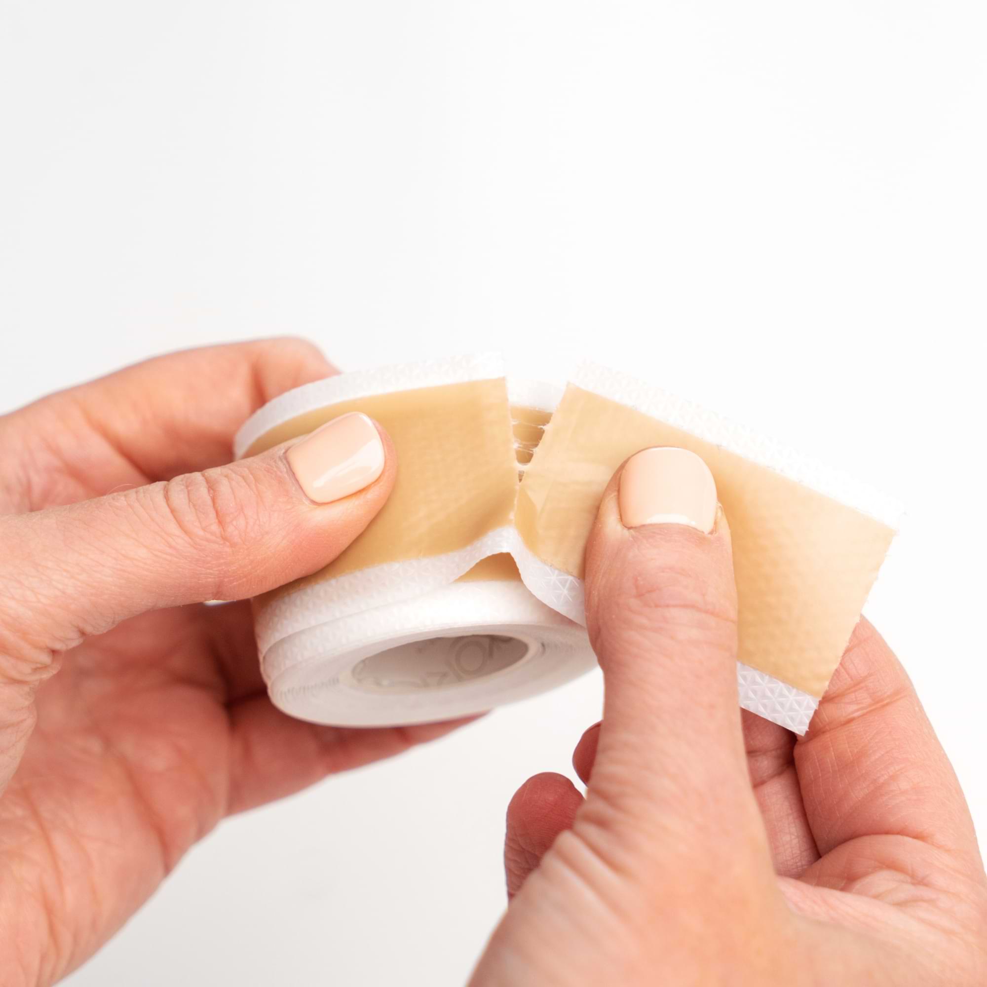 Close-up of hands tearing a strip of Nokori Scar Tape, illustrating the product’s easy-tear feature.