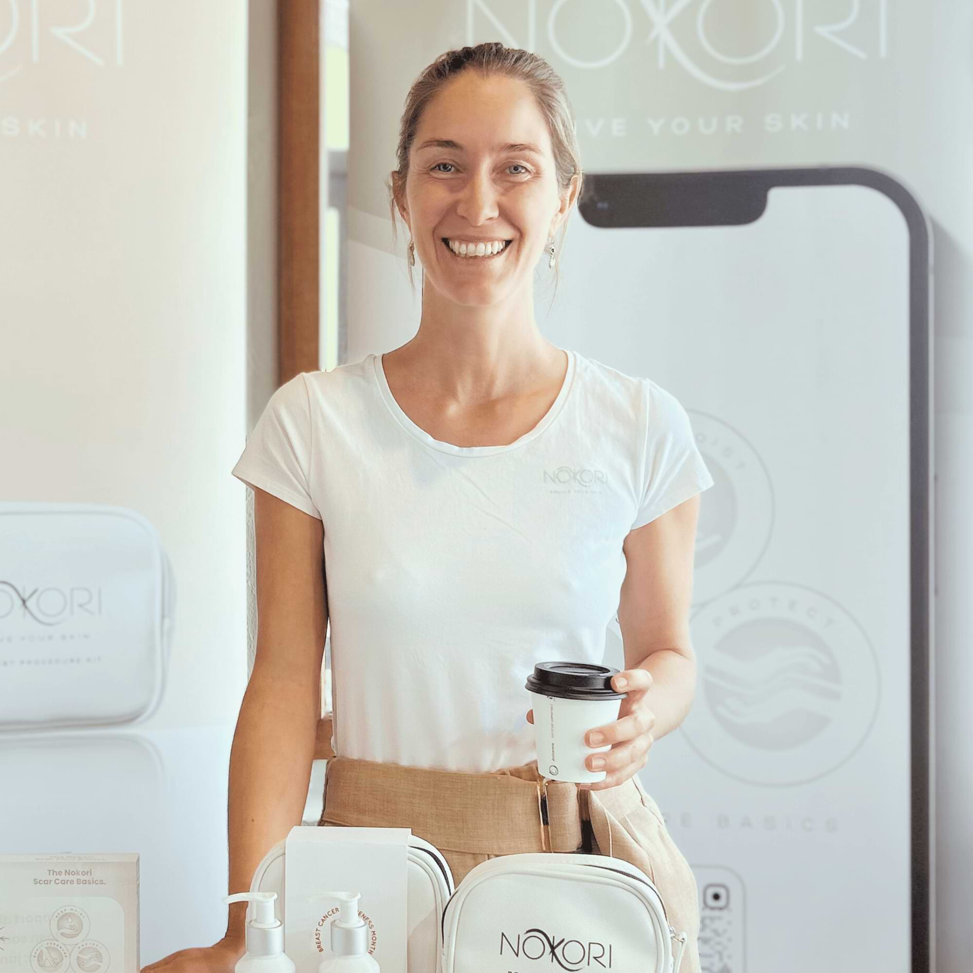 Max at a Nokori booth smiling, holding a takeaway coffee cup.