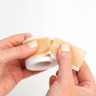 Close-up of hands tearing a strip of Nokori Scar Tape, illustrating the product’s easy-tear feature.